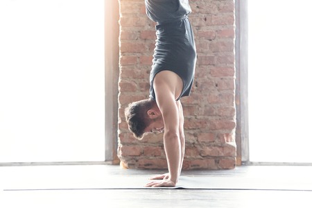Sport and yoga. Strong young athletic man doing exercise -Handstand against an urban background with...