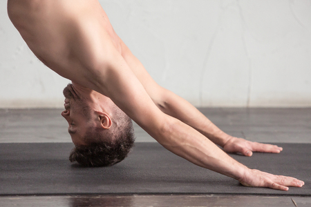Yoga. A young strong man doing yoga exercises. Studio shot over white wall background and black floor.の写真素材