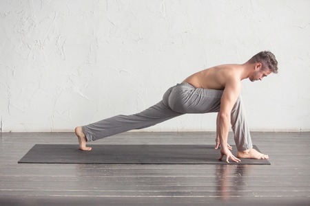 Yoga. A young strong man doing yoga exercises. Studio shot over white wall background and black...