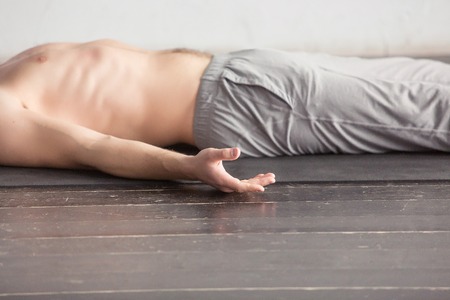 Yoga. Young men meditating on a wooden floor and lying in Shavasana pose. Yoga relax, meditating concept, close upの写真素材