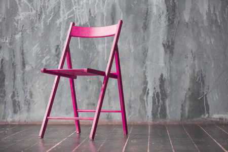 Pink wooden chair standing in front of a grey urban wall with mouldings on wooden black floor.の写真素材