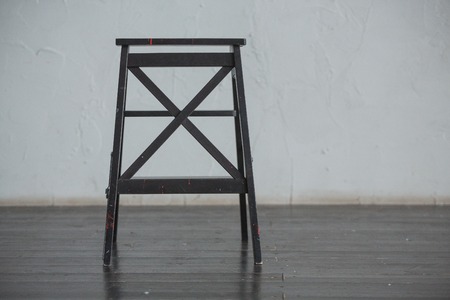 Black bar wooden chair standing in front of a grey urban wall with mouldings on wooden black floor.の写真素材