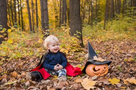 Portrait of Halloween smiling baby boy in dracula costume (cloak). Child in autumn forest looking at the falling leaves. Halloween pumpkin, witch hat, holiday conceptの写真素材