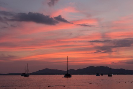 Sunset and dawn at sea against a backdrop of mountains and boatsの写真素材