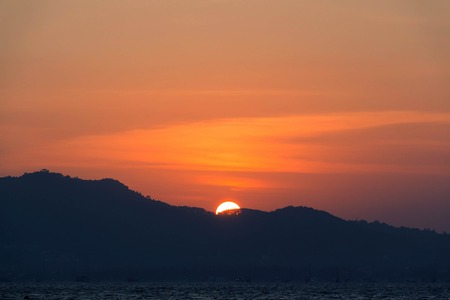 Sunset and dawn at sea against a backdrop of mountains and boatsの写真素材