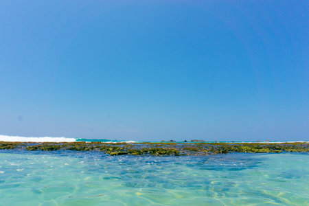 A strip of large stones and boulders goes into the sea, fencing the sandy beachの写真素材