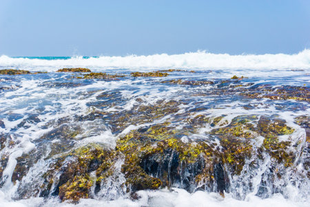 A strip of large stones and boulders goes into the sea, fencing the sandy beachの写真素材