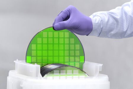 One of many silicon Wafer with semiconductors in plastic white storage box takes out by hand in gloves inside clean room.Green eco silicon wafers with glare.の写真素材