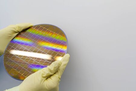 Silicon Wafer with microchips in the hands by gloves - A wafer is a thin slice of semiconductor material the fabrication of integrated circuits.Wafer with microchips.Rainbow on silicon wafers.Color silicon wafers with glare.の写真素材