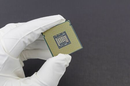 Hand in white glove holding a CPU computer processor microchip.Background is dark grey color.