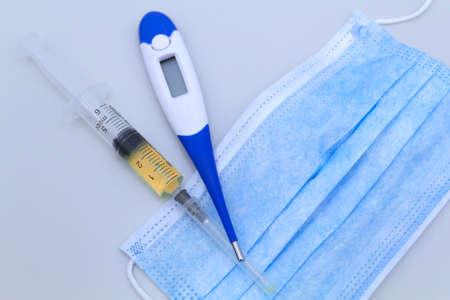 Syringe, protective mask and electronic thermometer on a grey background.Vaccination against the...