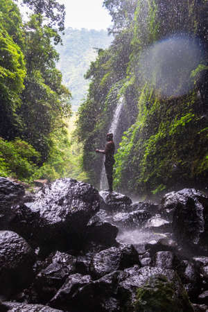 A man stands at the Sekumpul Great Waterfall in the deep rainforest of Bali Island, Indonesia.