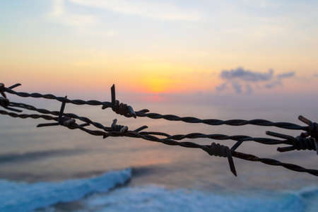 Barbed wire fence against sunset dark sky and sea.の写真素材