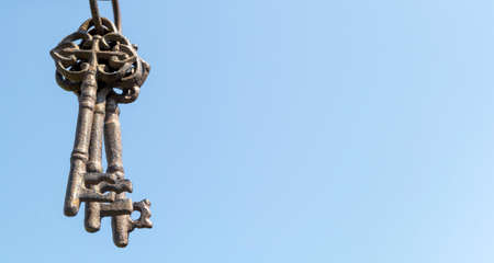 Three old rusty keys hang in the foreground against a blue skyの写真素材