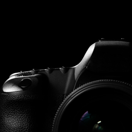 Image of a professional modern DSLR camera low key image  Modern DSLR camera with a very wide aperture lens on in a dark space. Top part of a camera is visible and the rest goes into the shadowの写真素材
