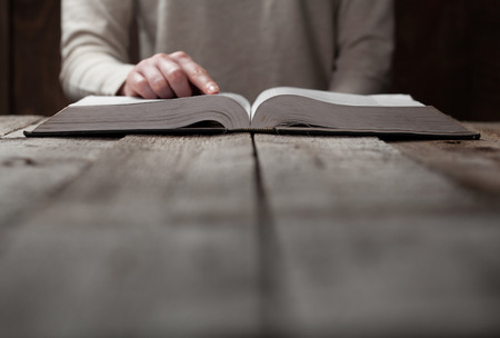 woman hands on bible. she is reading and praying over bible in a dark space over wooden tableの写真素材