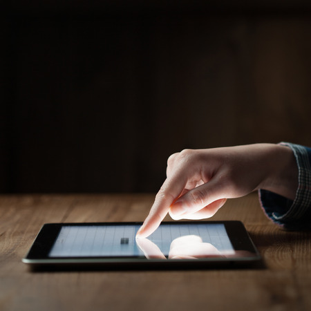 woman hand presses on screen digital tablet over wooden tableの写真素材