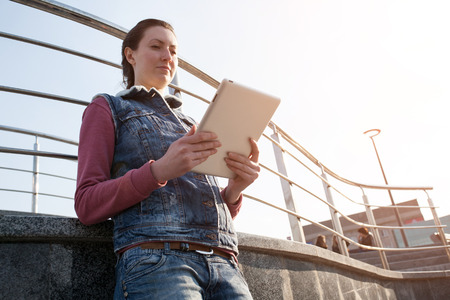 woman holding and using tablet pc outdoors in the city. She is wearing casual clothes and boots.の写真素材