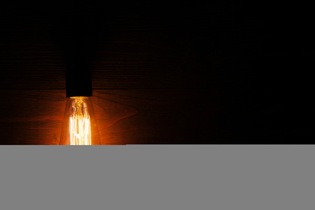 A classic Edison light bulb on wooden background switched on. retro edison light bulbの写真素材