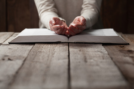 woman hands on bible. she is reading and praying over bible in a dark space over wooden tableの写真素材