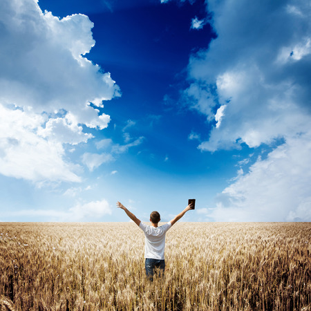 man holding up Bible in a wheat field