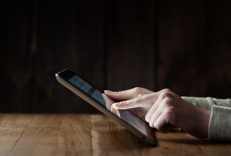 woman hand presses on screen digital tablet over wooden tableの写真素材