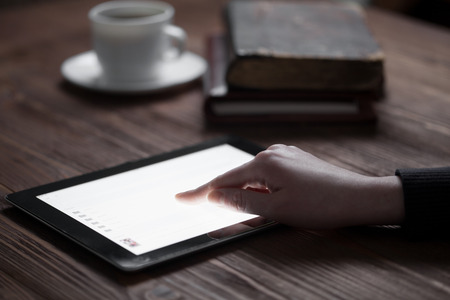 woman hand presses on screen digital tablet over wooden tableの写真素材