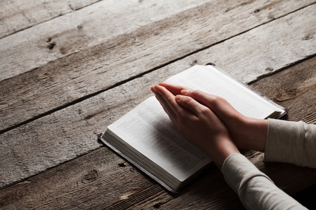 Woman hands praying with a bible in a dark over wooden tableの写真素材