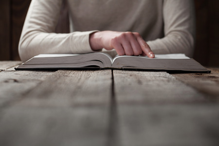 woman hands on bible. she is reading and praying over bible in a dark space over wooden tableの写真素材