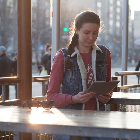 woman holding and using tablet pc outdoors in the city. She is wearing casual clothes and boots.の写真素材