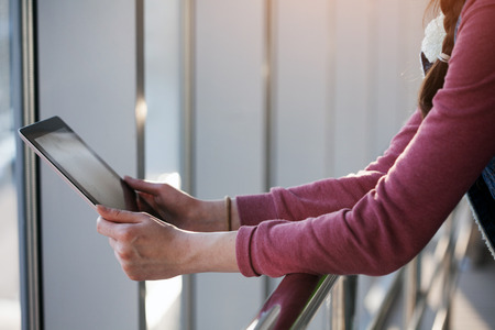 woman holding and using tablet pc outdoors in the city. She is wearing casual clothes and boots.の写真素材