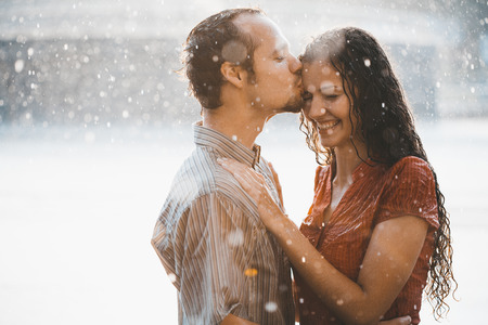 cople in love hugging and kissing under summer rainの写真素材