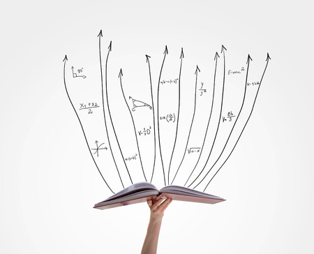 Human hand holding book with flying math formulasの写真素材