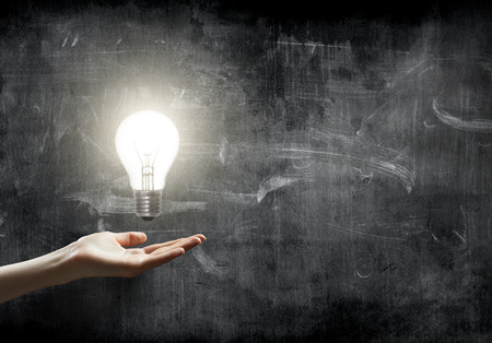 businesswoman holding Light bulb lamp on blackboard background with copy spaceの写真素材