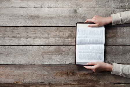 woman hands on bible. she is reading and praying over bible over wooden tableの写真素材