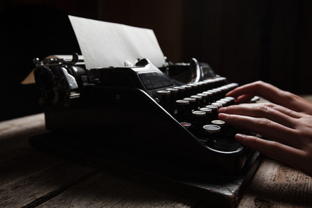 Hands writing on old typewriter over wooden table backgroundの写真素材