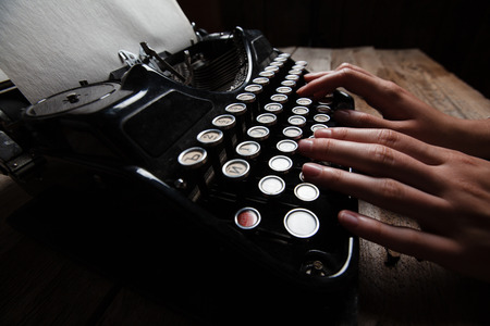 Hands writing on old typewriter over wooden table backgroundの写真素材