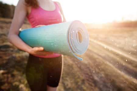 woman walking with a yoga mat outside during sunset n a rural area wearing sports wear and doing yogaの写真素材