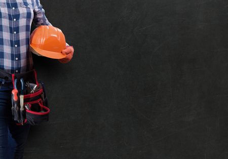 Worker woman with toolbelt and helmet against dark backgroundの写真素材