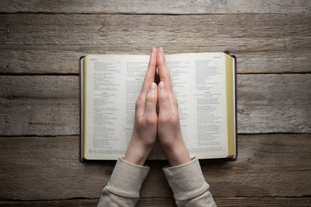 woman hands on bible. she is reading and praying over bible in a dark space over wooden tableの写真素材