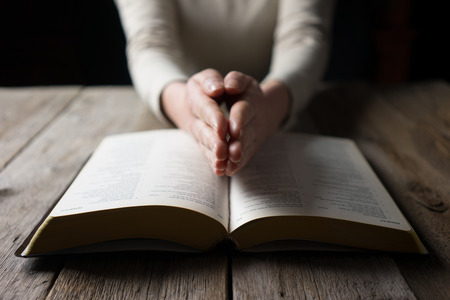 woman reading the bible in the darkness over wooden tableの写真素材