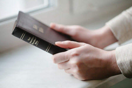 woman hands on bible. she is reading and praying over bible in a dark space over wooden tableの写真素材