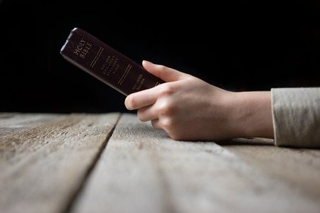 woman hands on bible. she is reading and praying over bible over wooden tableの写真素材