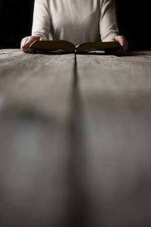 woman hands on bible. she is reading and praying over bible in a dark space over wooden tableの写真素材