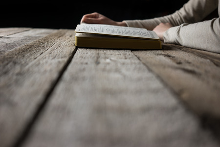 woman hands on bible. she is reading and praying over bible in a dark space over wooden tableの写真素材