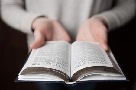 woman hands on bible. she is reading and praying over bible in a dark space over wooden tableの写真素材