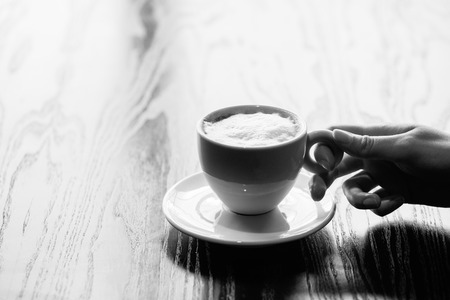 woman hands holding mug of hot coffee cup that standing on wooden tableの写真素材