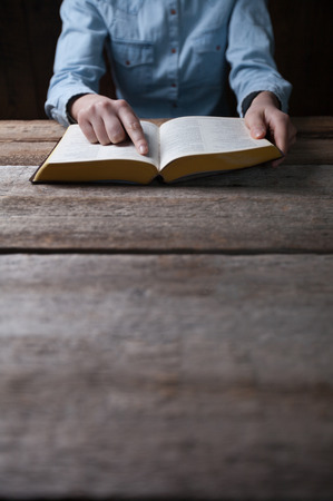Woman hands praying with a bible in a dark over wooden tableの写真素材