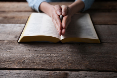 Woman hands praying with a bible in a dark over wooden tableの写真素材