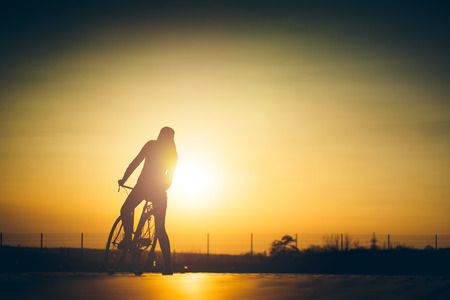 beautiful hipster girl with a bicycle on the road during sunsetの写真素材